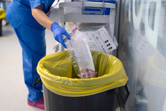 nurse wearing gloves disposing of medical waste in designated bin